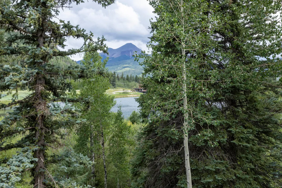 A panoramic view of a shimmering lake set against a dramatic backdrop of the San Juan Mountains and dense forest. The scene evokes peace and wonder, highlighting the striking natural surroundings visible from the property.