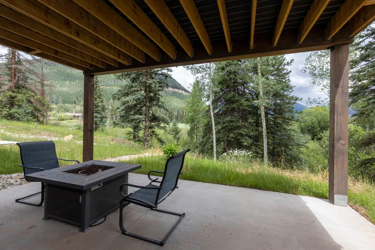 An inviting exterior gathering space with a fire pit surrounded by comfortable seating, set against a backdrop of natural greenery. The setup suggests relaxation, storytelling, and shared moments in the fresh mountain air.