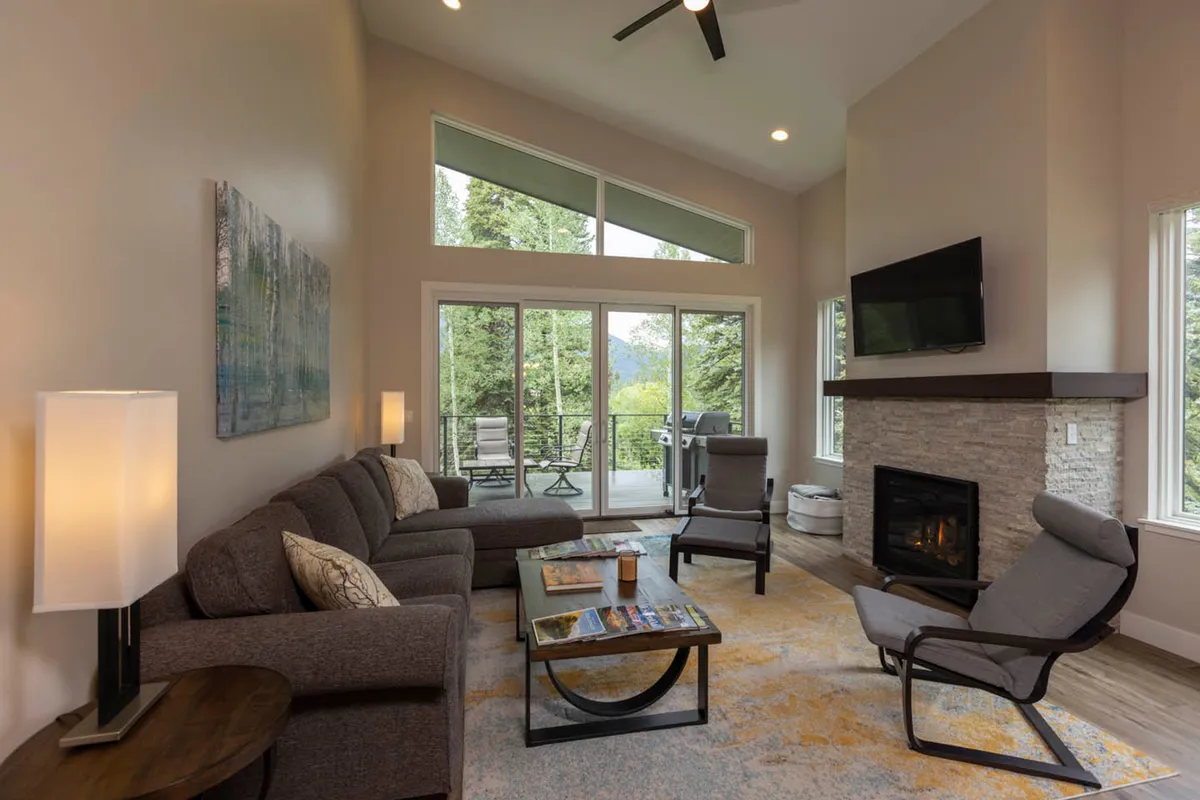 A modern family room featuring a cozy seating area by a sleek fireplace, with large windows framing tranquil views of the trees outside. The inviting setup makes it ideal for gathering, sharing stories, or winding down after a day of adventure.