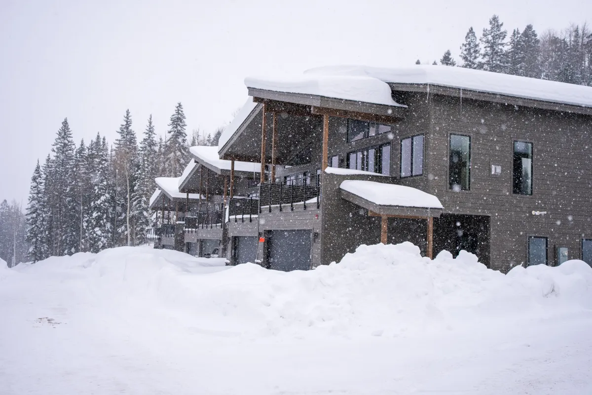 A picturesque winter scene featuring snow-covered buildings and trees, with a winding snowy pathway leading toward inviting resort accommodations. Soft light and undisturbed snow evoke both excitement for winter activities and the comfort of a cozy retreat.